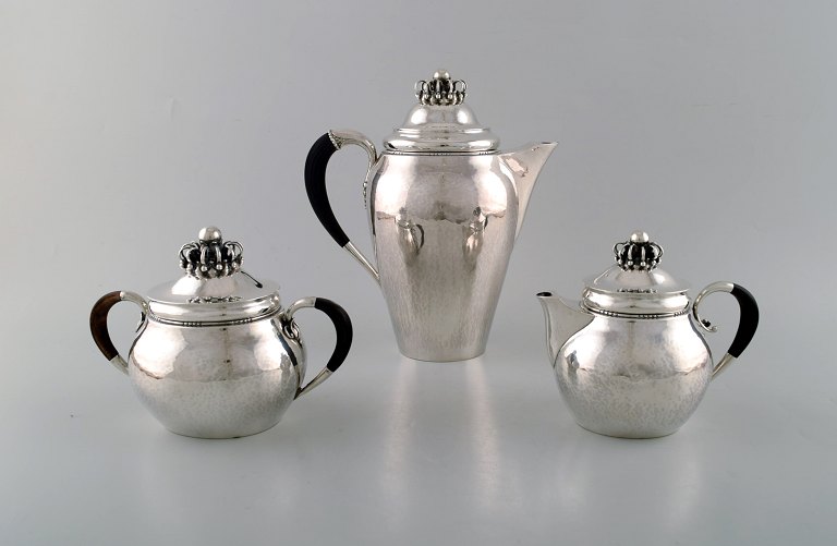 Rare Georg Jensen coffee service in sterling silver with ebony handles. Coffee pot, sugar bowl and cream pot. Lid shaped as royal crown. Dated 1915-30.