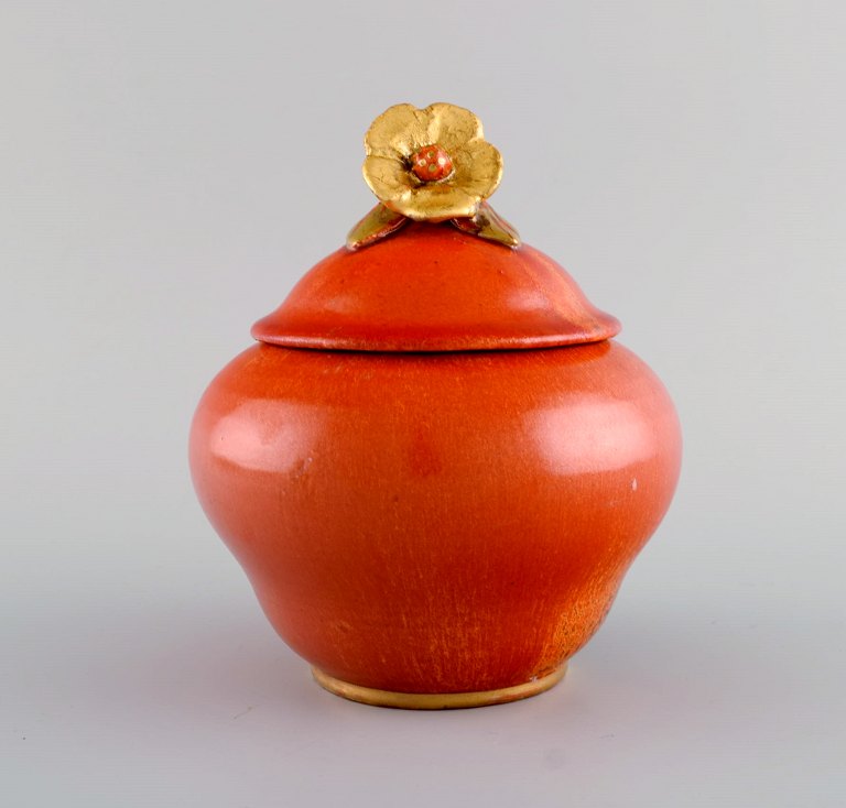 Nils Emil Lundström (1865-1960) for Rörstrand. Antique lidded jar in glazed ceramics. Beautiful orange glaze and flower in gold on the lid. Early 20th century.