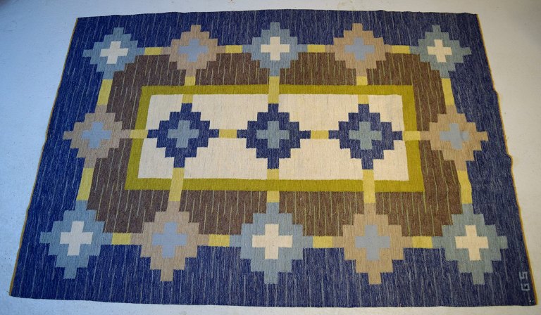 Swedish textile designer. Large hand-woven RÖLAKAN rug in pure wool with geometric fields in olive green, brown, blue, and sand-colored shades. Mid-20th century.
