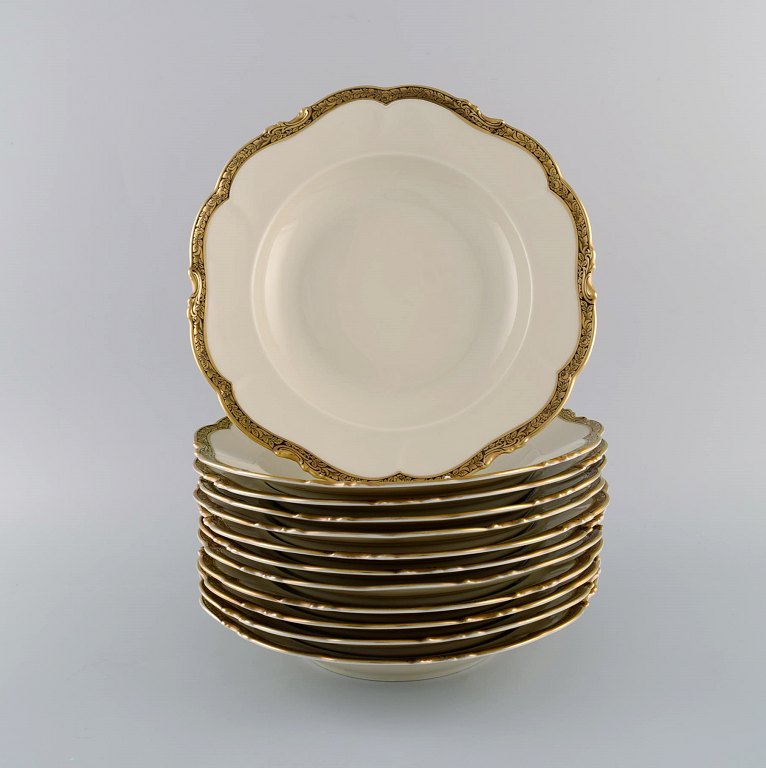 KPM, Berlin. Tolv Royal Ivory dybe tallerkener i cremefarvet porcelæn med gulddekoration. 1920