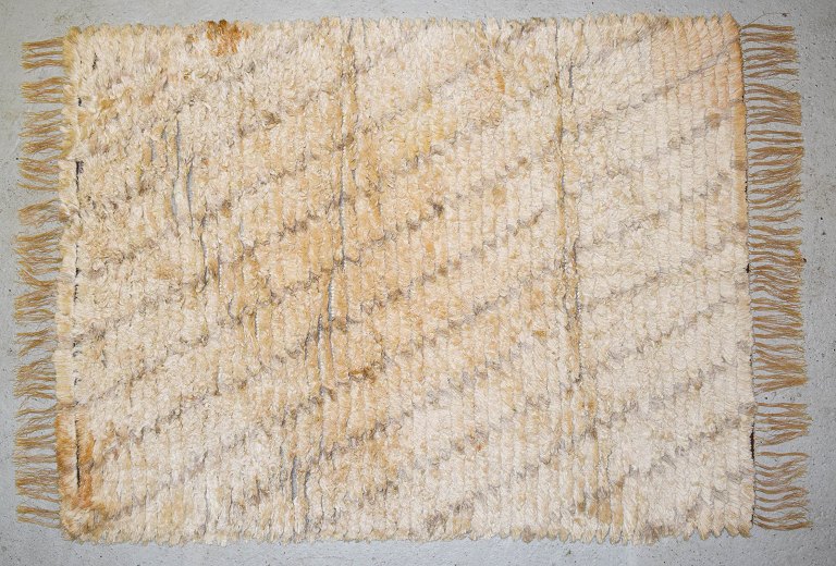 Svensk tekstildesigner.
Ryatæppe med frynser i ren uld i lyse nuancer.