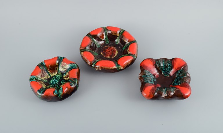 Vallauris, France, three ceramic bowls in brightly colored glazes in red and green on a dark base.